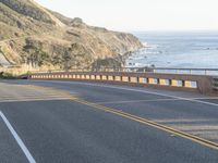 the man is riding his motorcycle on the side of the road beside a cliff overlooking the ocean