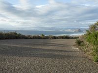 a bench overlooking the ocean from a parking lot with an rv parked beside it on a beach road