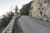 a lone mountain bike riding down a winding road by a large rock wall, overlooking the ocean