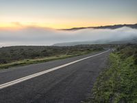 a motorcycle is parked on the side of a hill with fog in the air and low hills