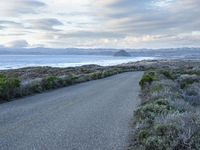 a long paved road beside the ocean on the other side of the beach, a lone motorcycle rider is riding along