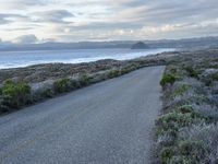 a long paved road beside the ocean on the other side of the beach, a lone motorcycle rider is riding along