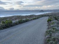 a long paved road beside the ocean on the other side of the beach, a lone motorcycle rider is riding along