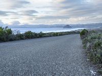 a long paved road beside the ocean on the other side of the beach, a lone motorcycle rider is riding along