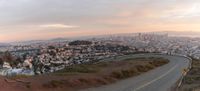 a curve in the road above the city of san francisco in the distance are tall buildings and green shrubs