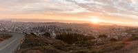 a curve in the road above the city of san francisco in the distance are tall buildings and green shrubs