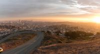 a curve in the road above the city of san francisco in the distance are tall buildings and green shrubs