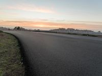 the empty road is next to the water and mountains at sunset time, as if riding a motorbike