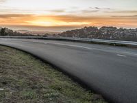 the empty road is next to the water and mountains at sunset time, as if riding a motorbike