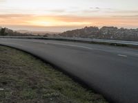 the empty road is next to the water and mountains at sunset time, as if riding a motorbike