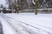 a street full of snow with several trees lining the side of it and fenced in