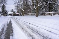 a street full of snow with several trees lining the side of it and fenced in