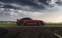 the sport car is driving on the country road in front of the water area and the cloudy sky