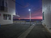 there is an empty parking lot near the ocean at night time, the street lights brighten up the street and sky