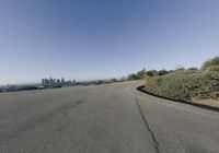 an empty street with trees and buildings in the background by a hill top and hills