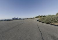 an empty street with trees and buildings in the background by a hill top and hills