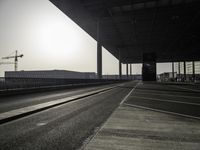 a deserted street with construction cranes in the background at sunset by a freeway bridge over a parking lot