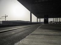 a deserted street with construction cranes in the background at sunset by a freeway bridge over a parking lot