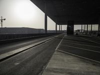 a deserted street with construction cranes in the background at sunset by a freeway bridge over a parking lot