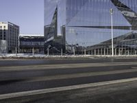 an empty city street in front of a glass building with a statue on the sidewalk