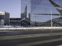 an empty city street in front of a glass building with a statue on the sidewalk