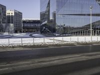 an empty city street in front of a glass building with a statue on the sidewalk