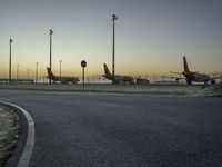 a bunch of airplanes are parked at an airport gate fenced off area next to a paved road