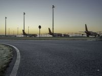 a bunch of airplanes are parked at an airport gate fenced off area next to a paved road