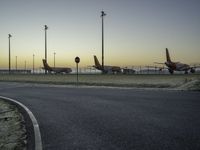 a bunch of airplanes are parked at an airport gate fenced off area next to a paved road