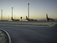 a bunch of airplanes are parked at an airport gate fenced off area next to a paved road