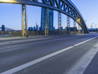this city road has a bridge that spans it and there are buildings in the background