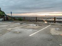 a lone person in the parking lot is near a fence with a view to a city