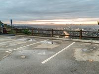 a lone person in the parking lot is near a fence with a view to a city