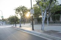 there is a sun shine shining through the streetlight above a road and sidewalk with a person riding their motorcycle behind it