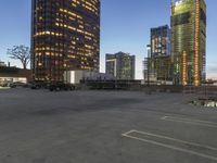 several tall buildings sit in an empty parking lot, with two parked trucks next to each other