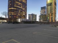 several tall buildings sit in an empty parking lot, with two parked trucks next to each other