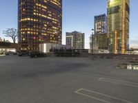 several tall buildings sit in an empty parking lot, with two parked trucks next to each other