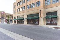 a street near a large building with a store front and several shops around it on the other side of the street