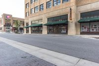 a street near a large building with a store front and several shops around it on the other side of the street