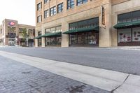 a street near a large building with a store front and several shops around it on the other side of the street