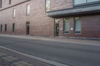 the entrance to the brick building is empty on the street, as a person walks down a sidewalk