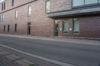 the entrance to the brick building is empty on the street, as a person walks down a sidewalk