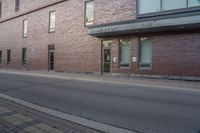 the entrance to the brick building is empty on the street, as a person walks down a sidewalk