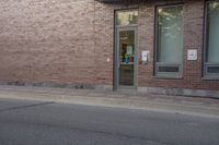 the entrance to the brick building is empty on the street, as a person walks down a sidewalk