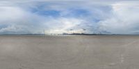 the person is skateboarding on a flat surface area next to water and clouds,