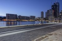 a street with lots of buildings next to some water and a bench with chairs under it