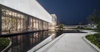 a walkway on a courtyard at night with water in foreground and a building behind