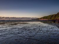 a person is standing near the water at sunset on the beach in the surf at low tide