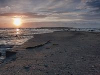 an empty sandy beach at sunset with a dead log by the ocean shore and another small body of water on it