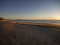 a bench facing the water at sunset on a deserted street next to a beach and ocean